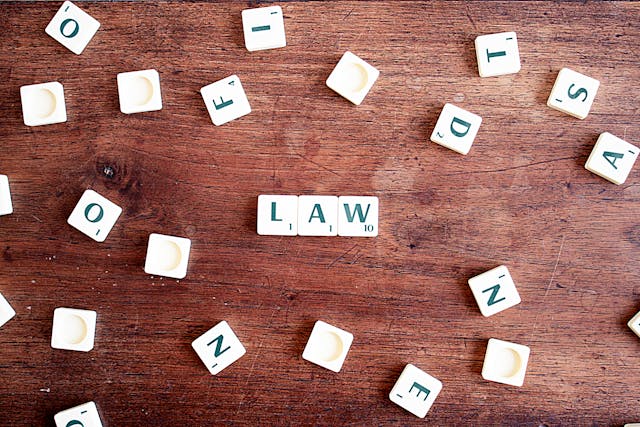 scrabble tiles scattered across a wooden table with three in the middle that spell out "law"